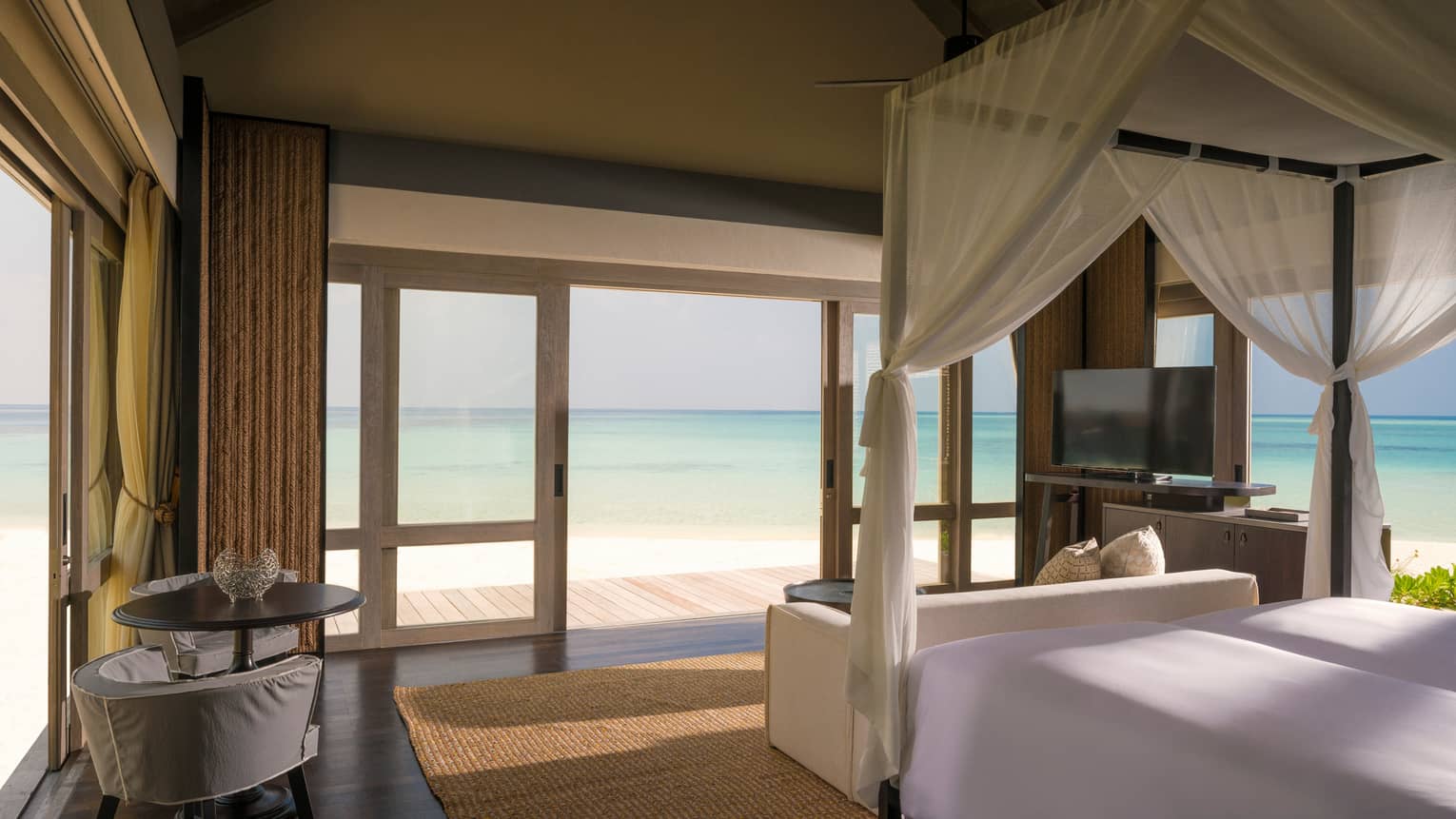 Beach Villa bedroom with white canopy bed by sliding doors to patio, lagoon views