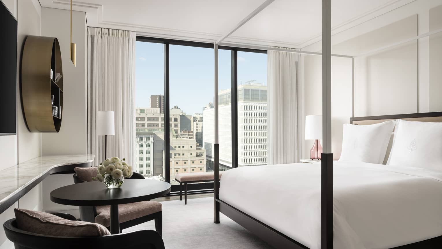 Superior King Room with modern four-poster bed in all-white room with conversation vignette and floor-to-ceiling windows with city views