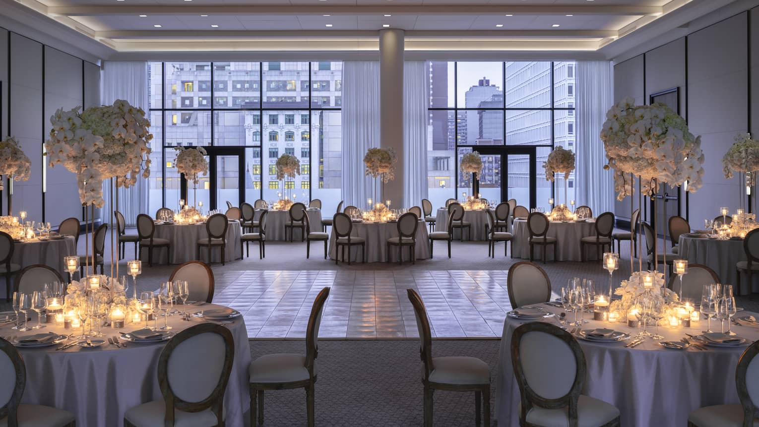 Palais des Possibles Ballroom with floor-to-ceiling windows, round tables with candles and large floral displays