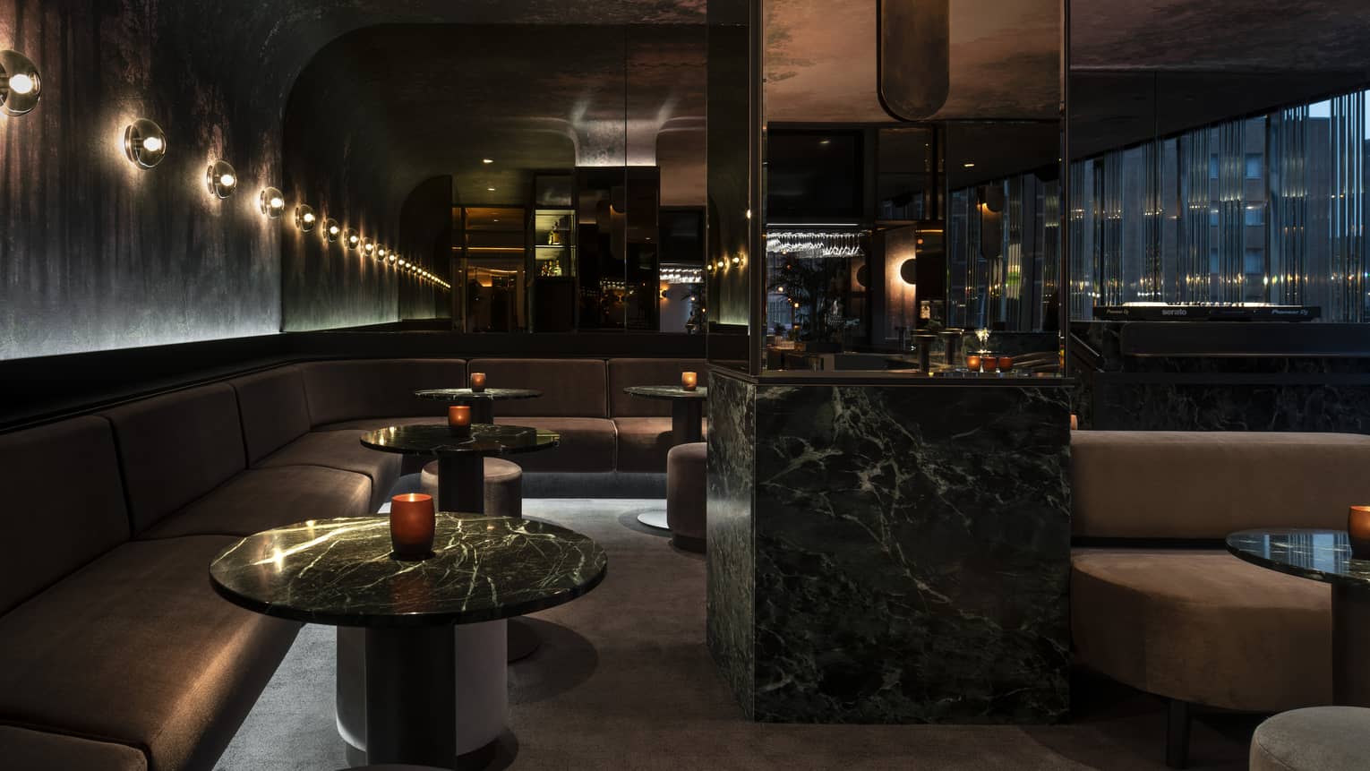 Dimly lit MARCUS Bar features rounded mauve banquets and black marble cocktail tables