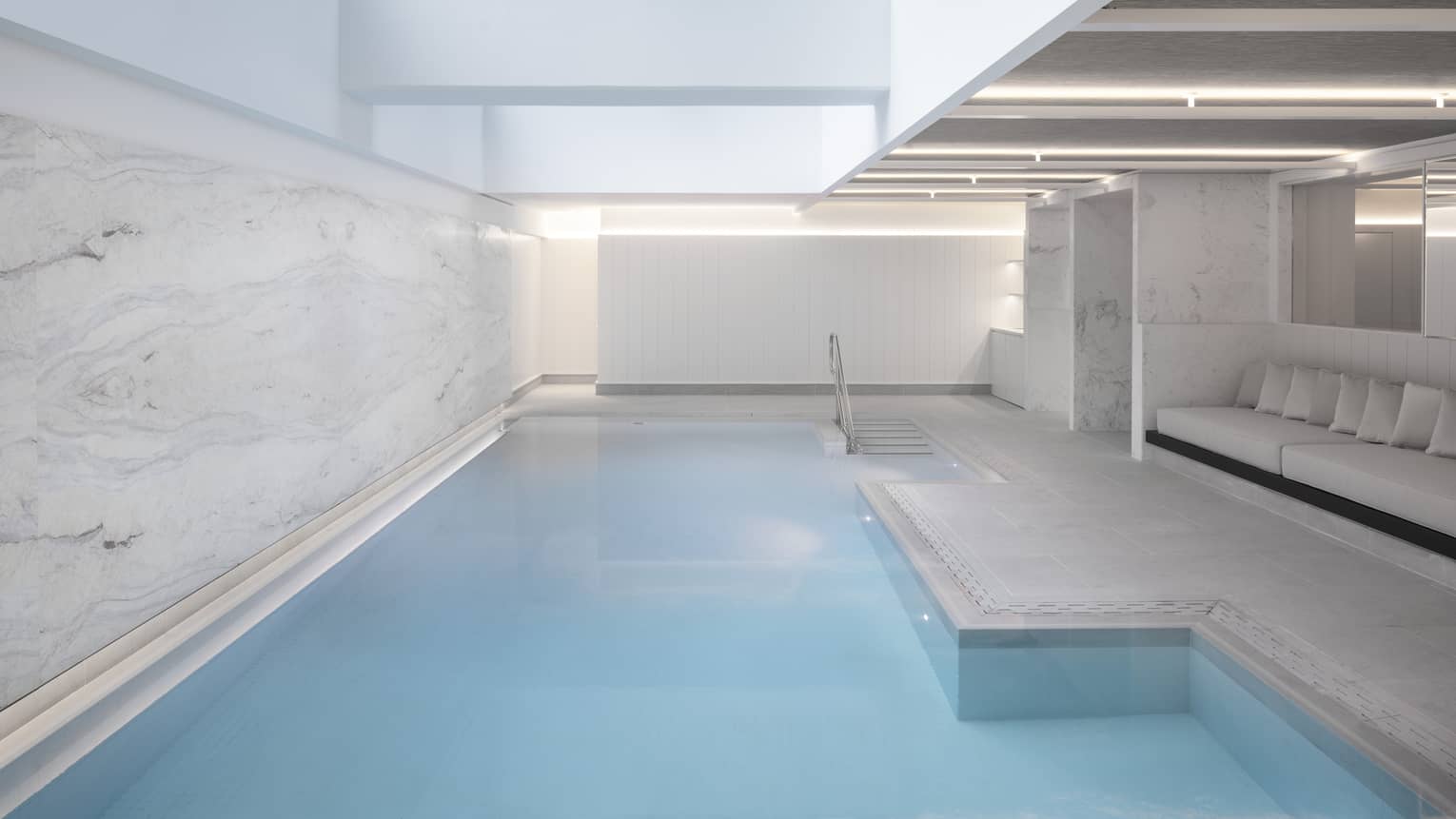 Indoor pool at spa, banquet of seating on one side, marbled wall on other 