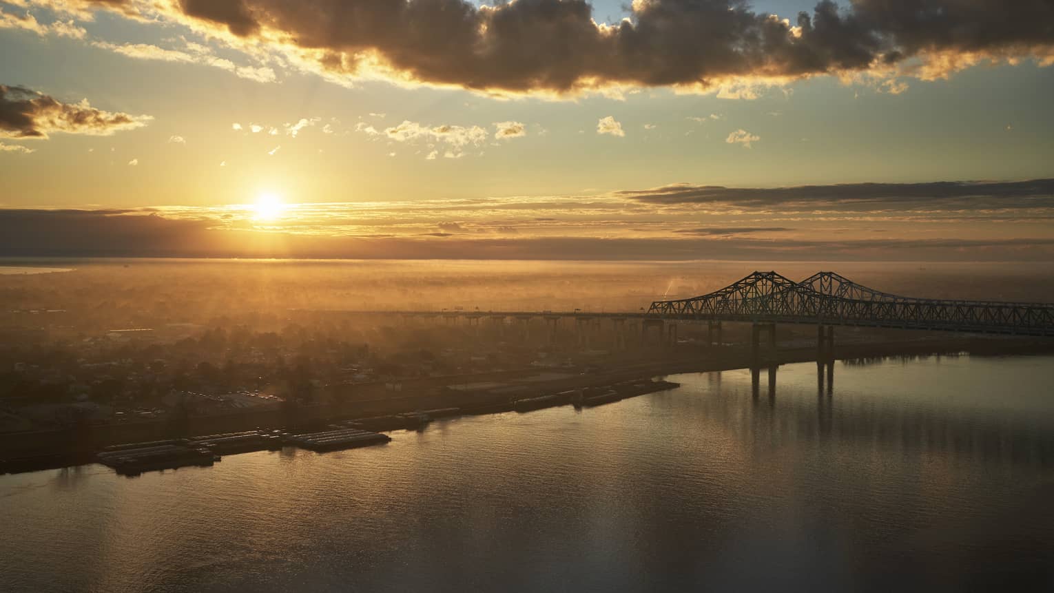 A sunrise near New Orleans bridge crossing a river.