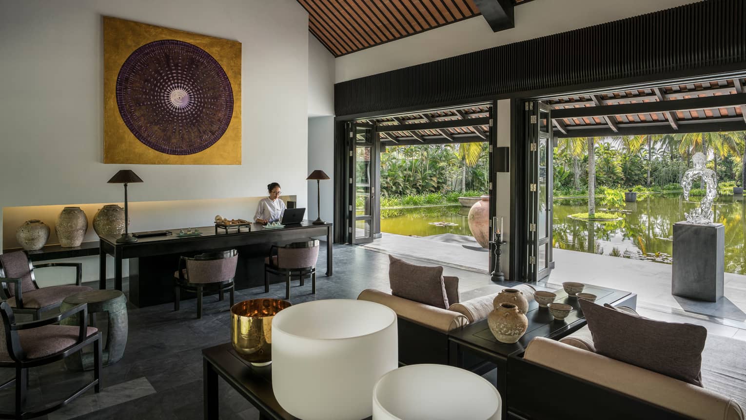 Woman at reception desk in open-air spa lobby with sofas, art 