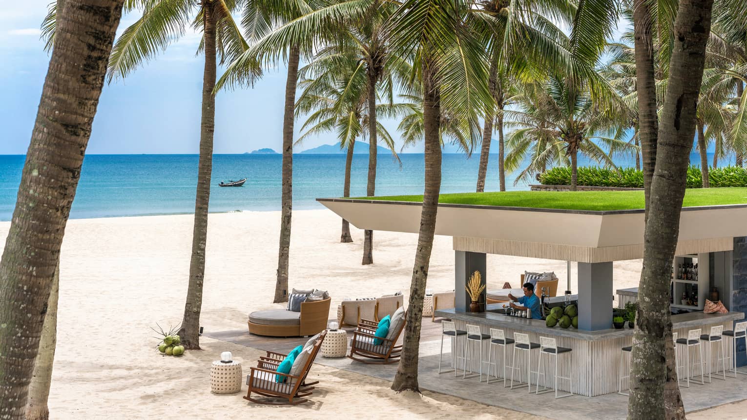 Bartender mixes drink at square stand-alone Beach Bar gazebo under palms on white sand