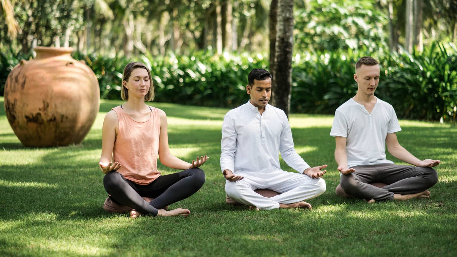Two men and a woman practise meditation yoga outdoors on lawn