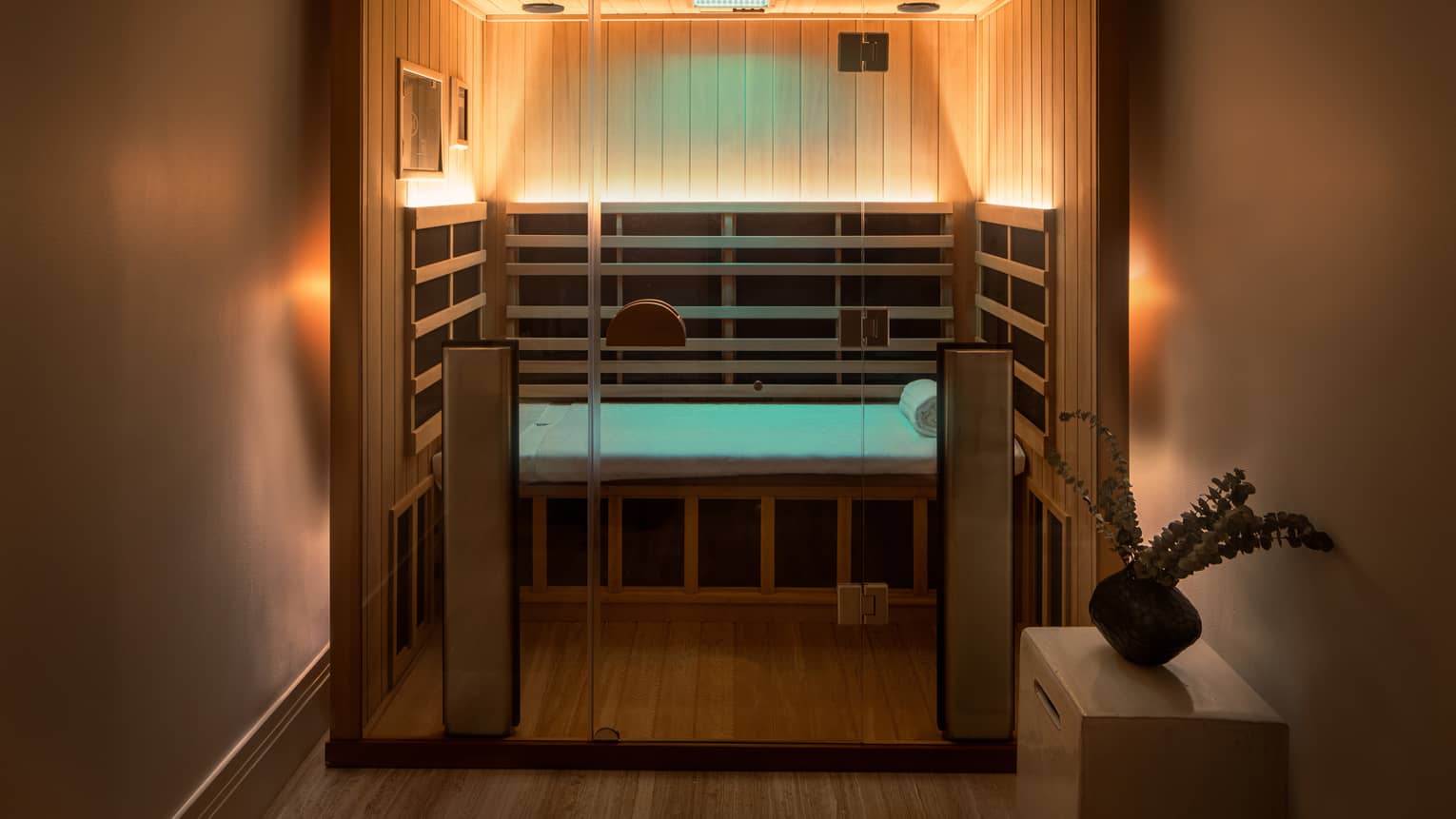 Wooden infrared sauna with lowlighting, side table with vase of eucalyptus 
