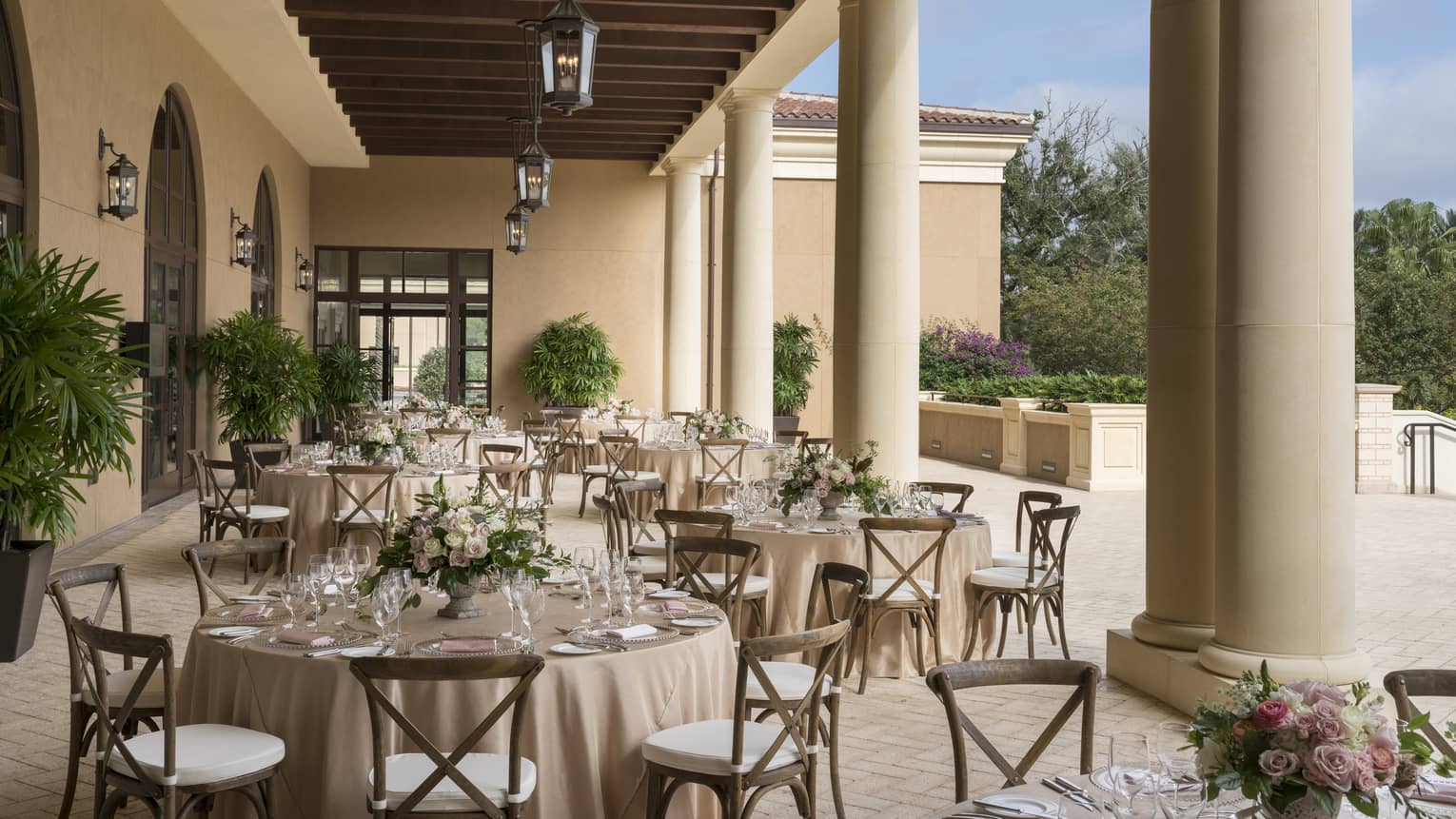 The Grand Ballroom Terrace is ready for guests with circular tables set with a cream table cloth, clear glass plates and tableware and a green floral arrangement in the center