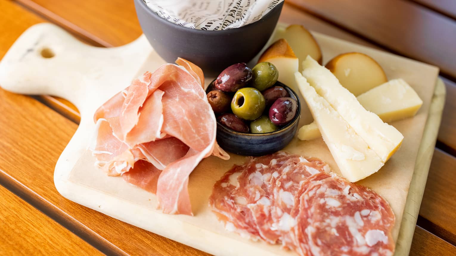 A selection of cheese and charcuterie on a wooden board.