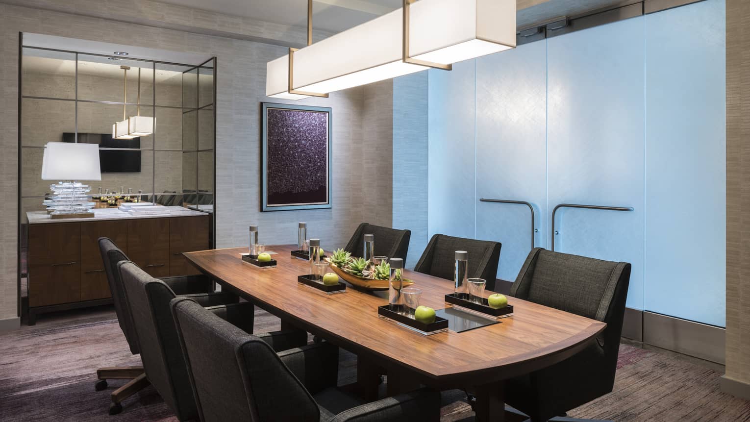 Wood boardroom meeting table with black executive chairs under modern light, glass wall