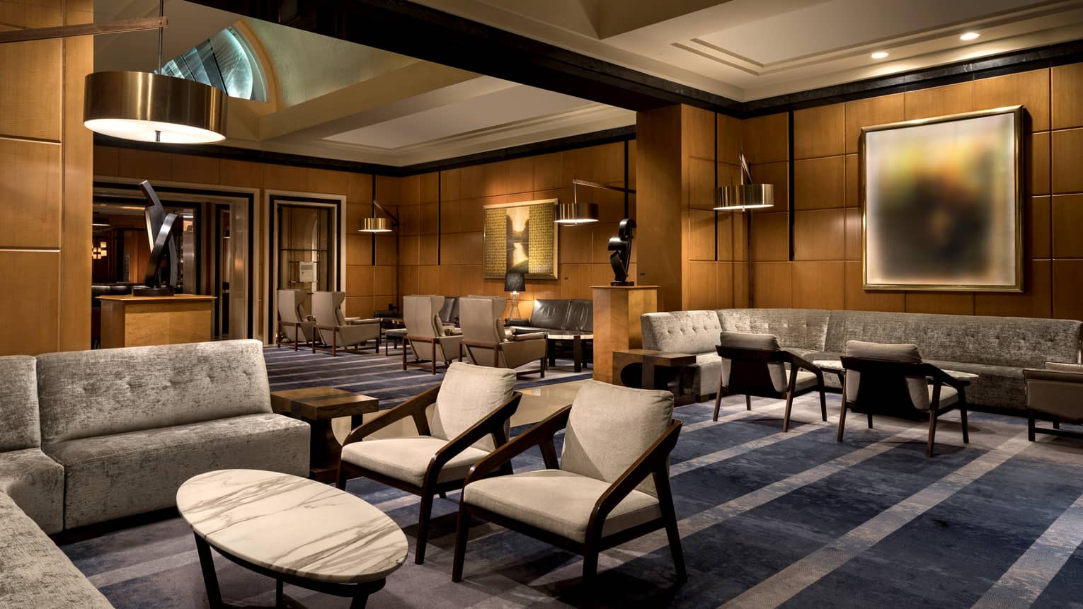 A lounge and lobby area with dark blue carpeting, grey chairs and sofa, and wood walls.