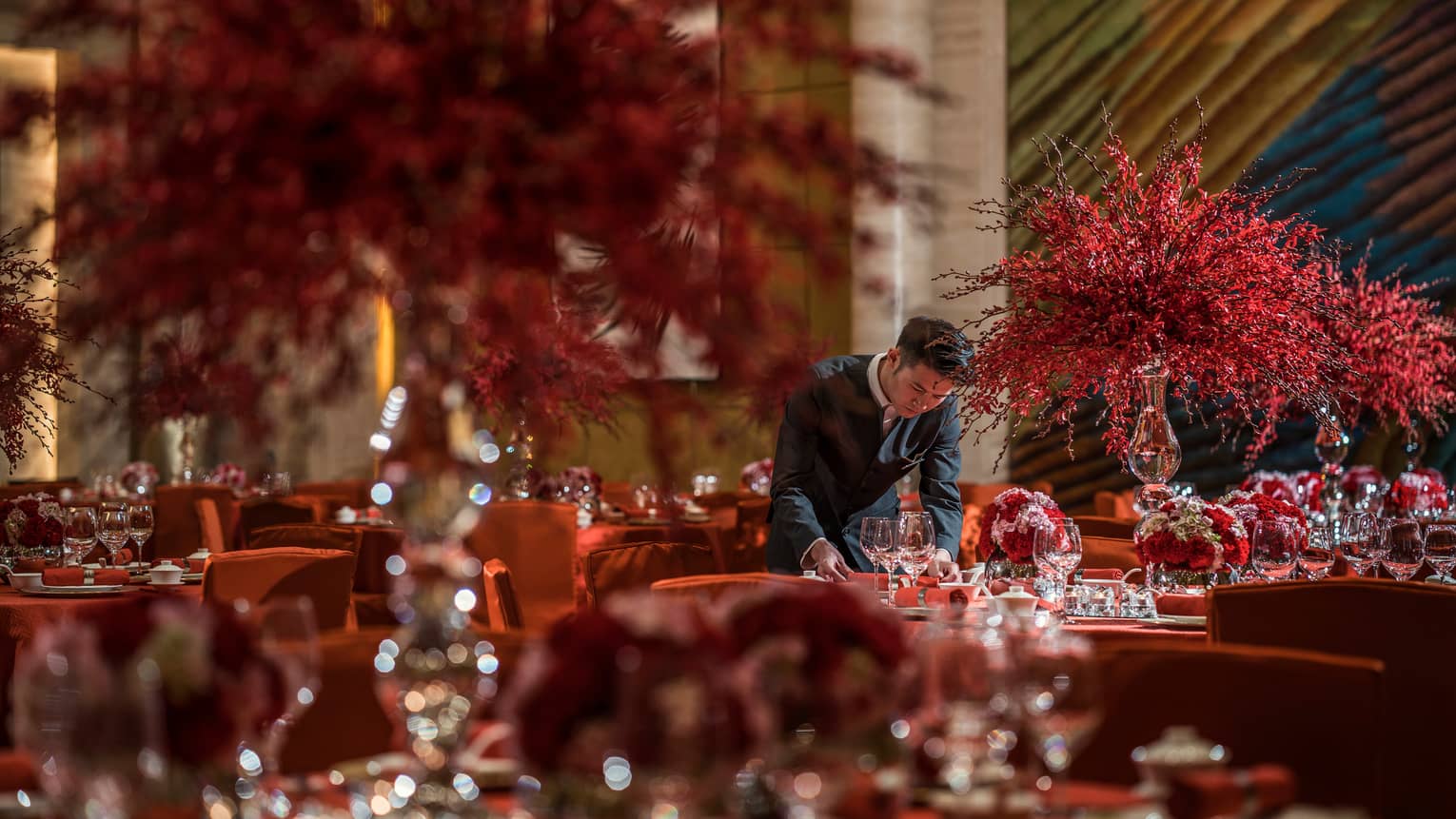 Hotel staff sets banquet tables with large red flower arrangements