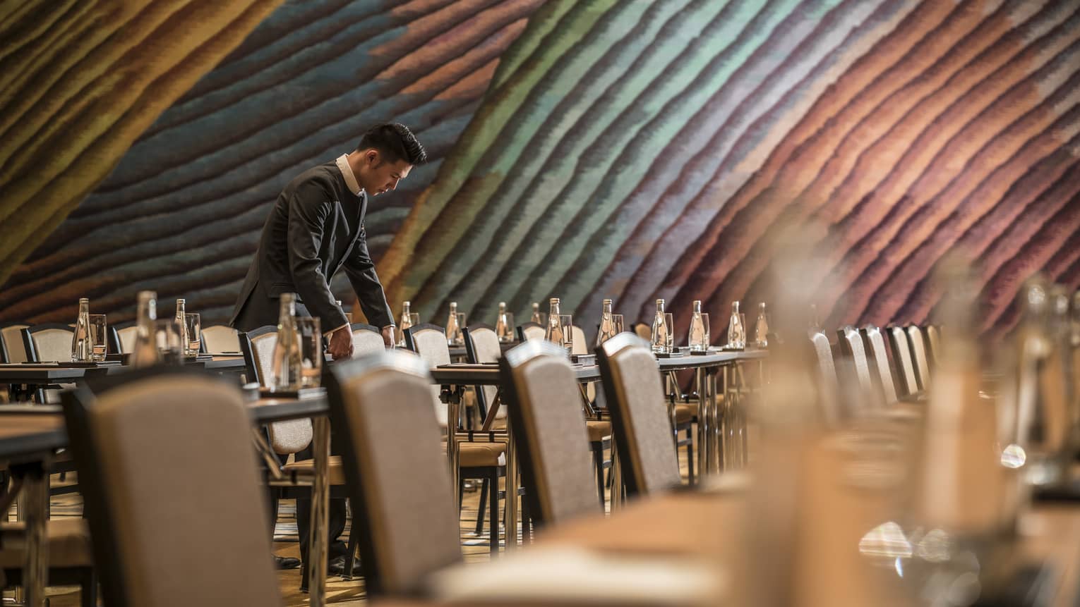 Hotel staff sets long conference meeting tables under colourful accent wall