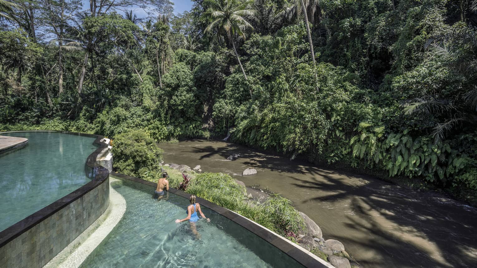 Hotel guests swimming in a pool, overlooking a river in Bali