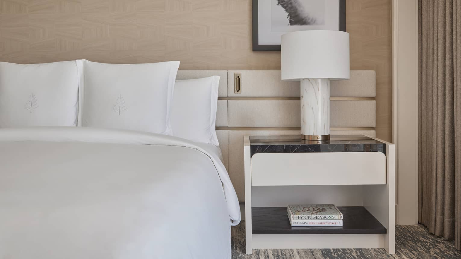 A bed in a guest room with a side table and lamp.