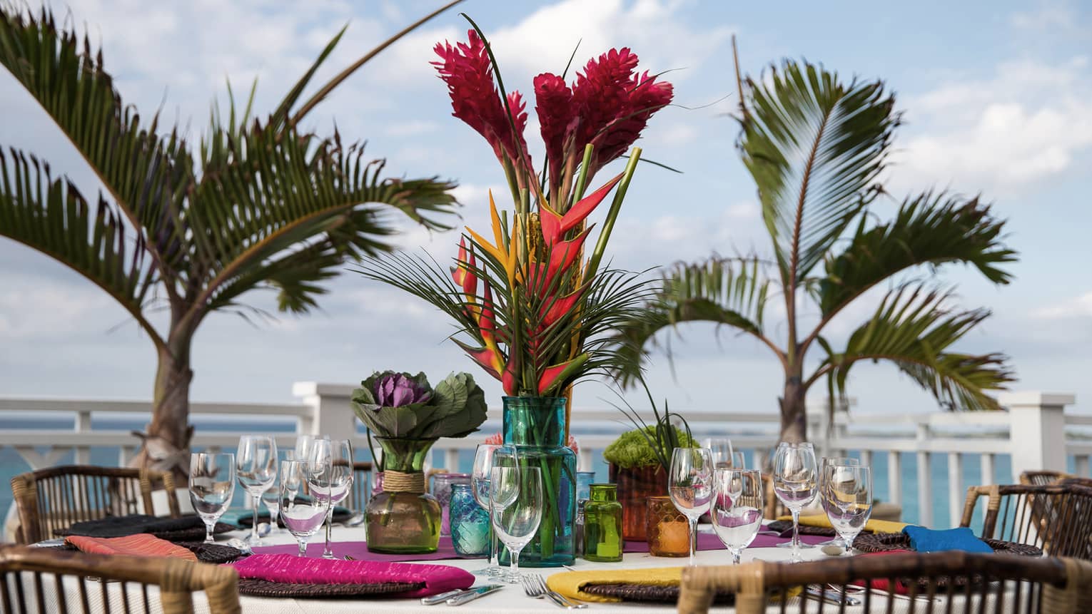 Brightly colored place settings and flowers adorn a a table, outside beside palm trees