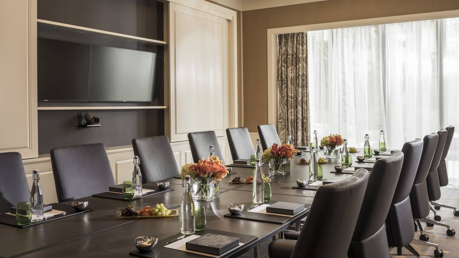 Long boardroom table set with glass bottles of water, flowers in bright meeting room