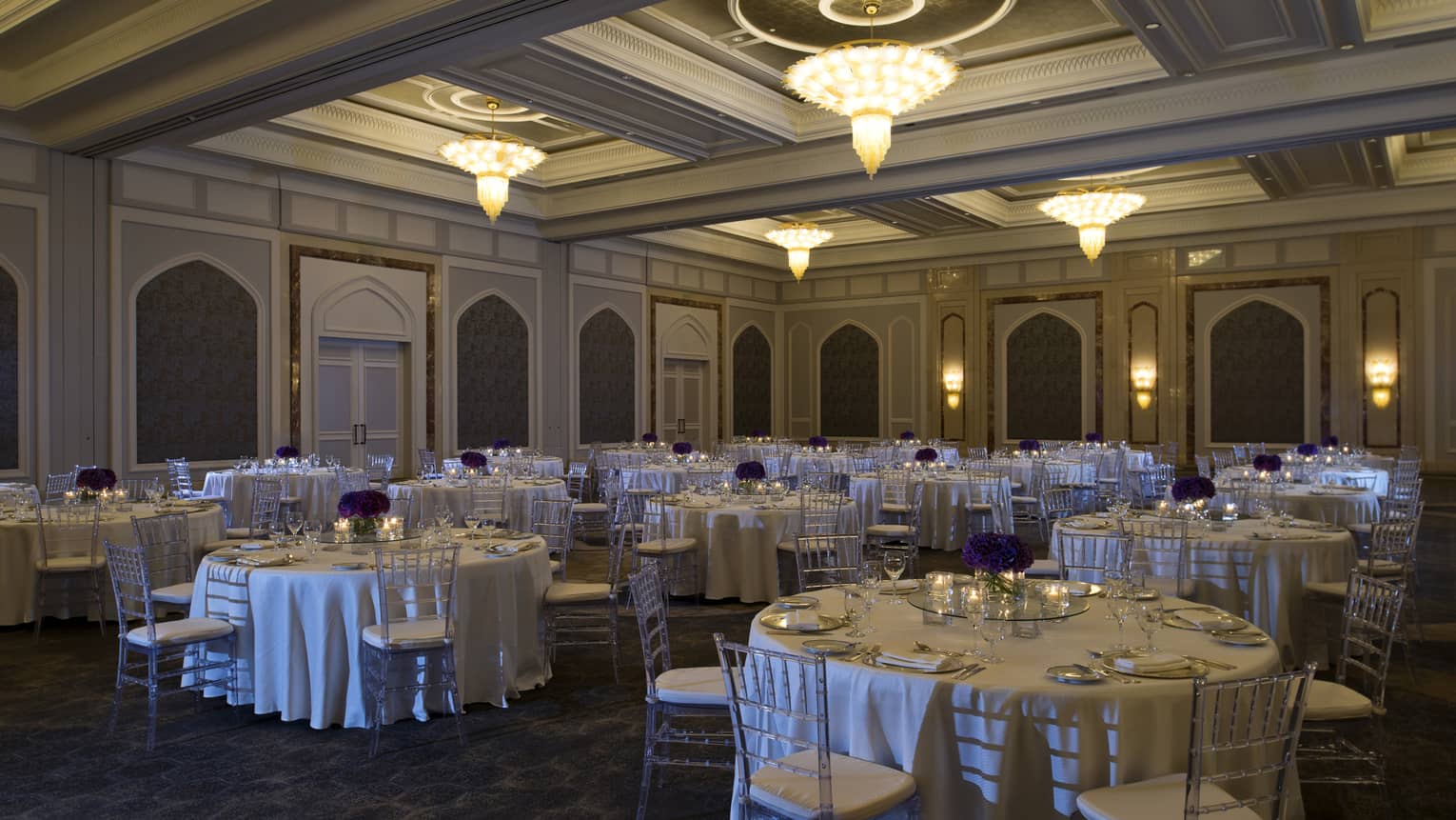 Ballroom with round banquet tables, chairs under small chandeliers 