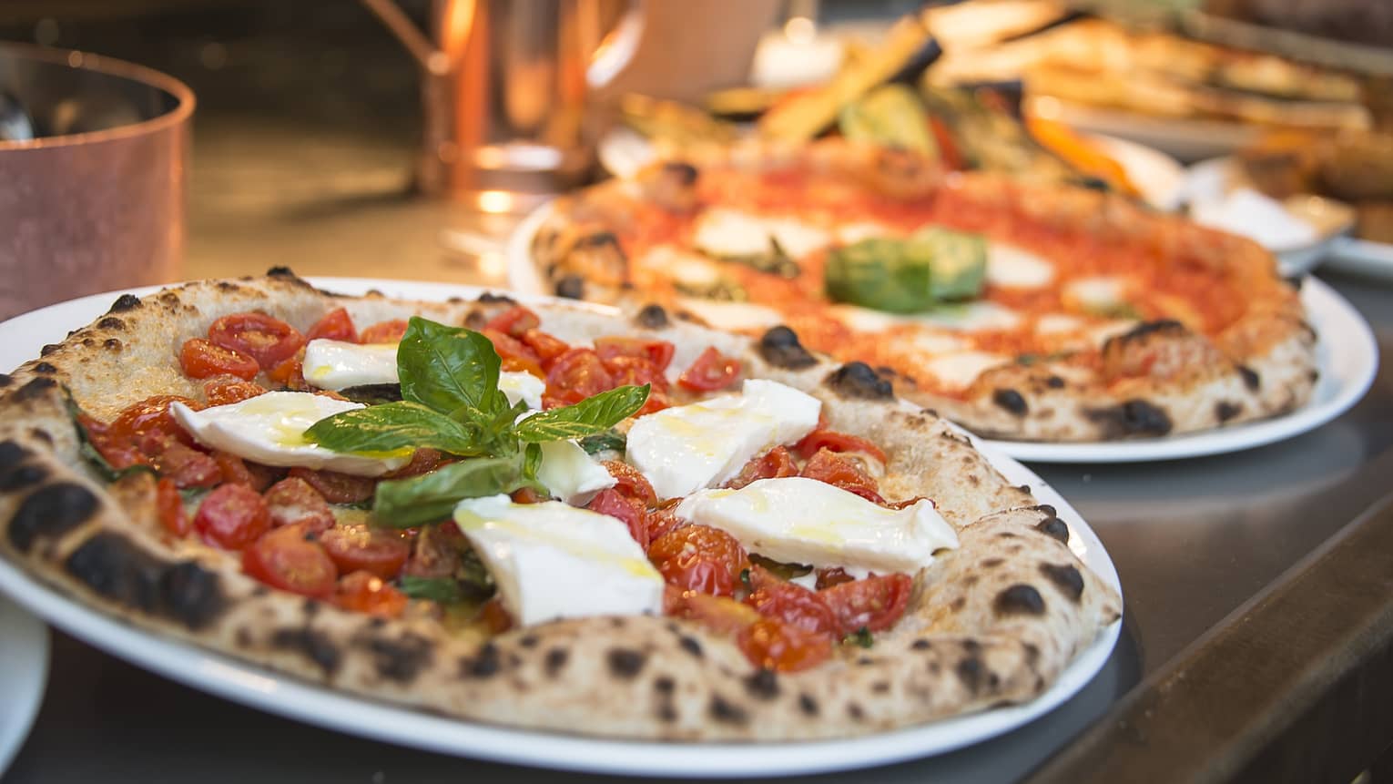 Two rustic pizzas with fresh basil leaves on counter 