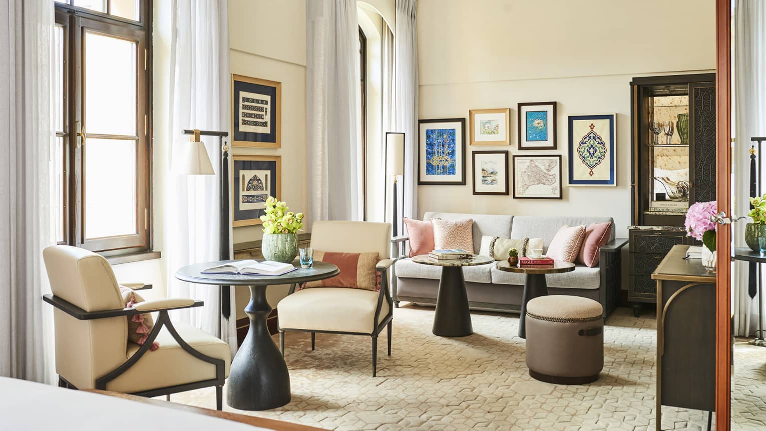 Hotel suite's living area, featuring a round table with two upholstered chairs, sofa, two coffee tables, colourful framed prints on the wall and two French windows