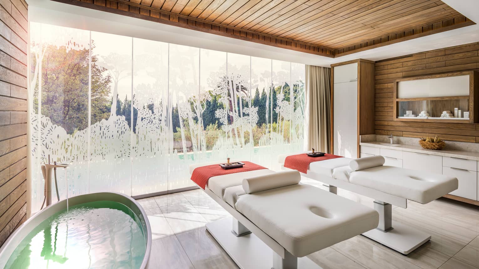 Couples Spa Suite with two side-by-side massage tables beside round tub, by floor-to-ceiling window