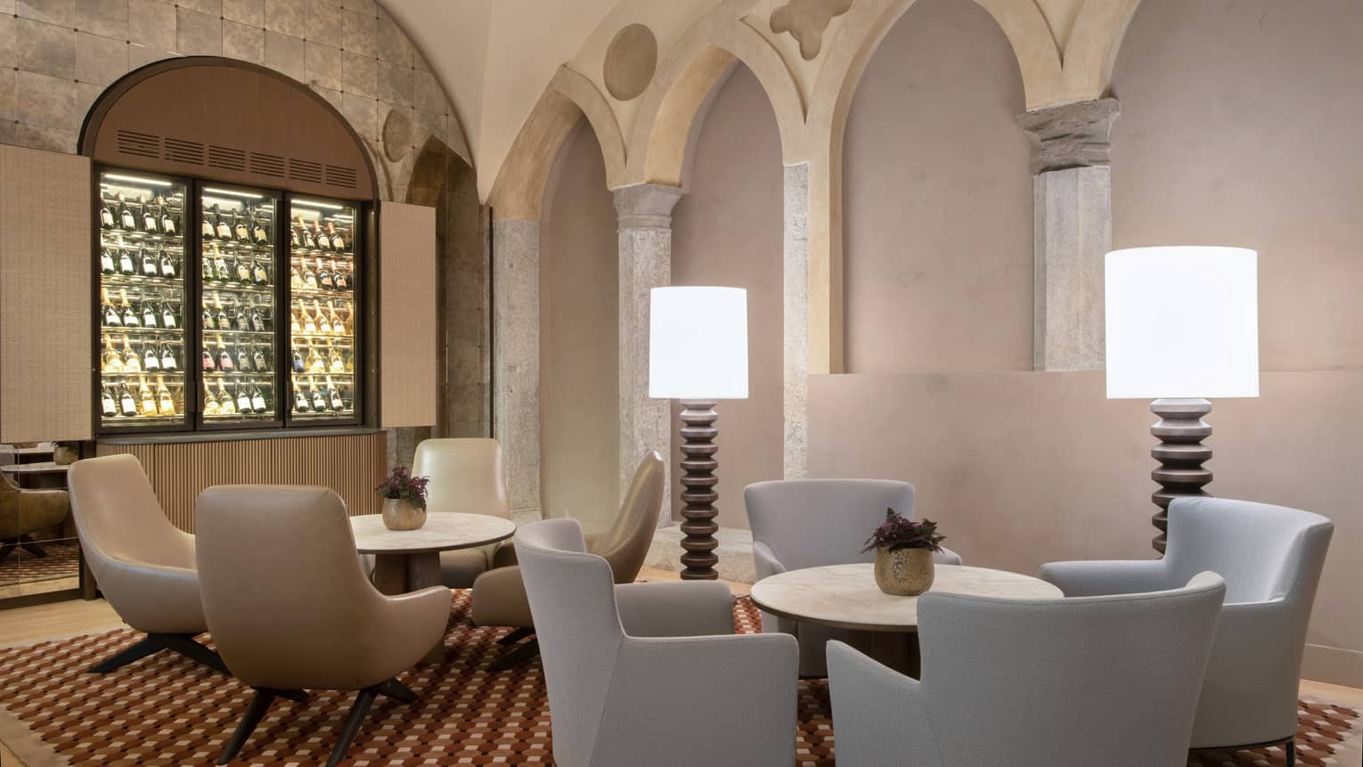 Camino lobby bar with neutral modern round tables and chairs, two floor lamps, arches in backdrop