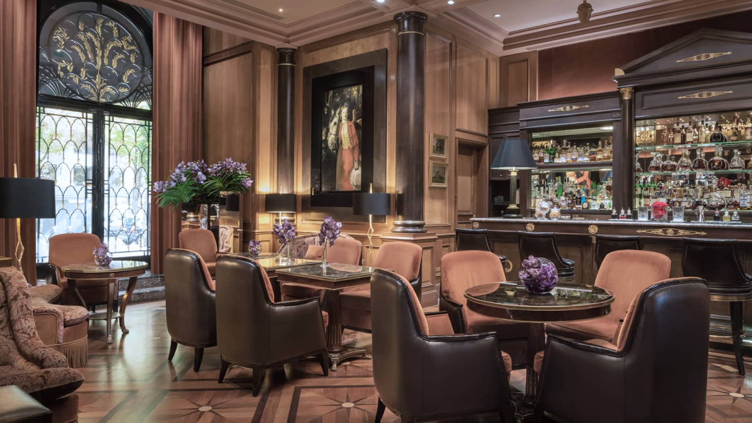 Bar with brown leather barstools and lounge area with rust-colored club-style seating, black lamps and purple flower arrangements