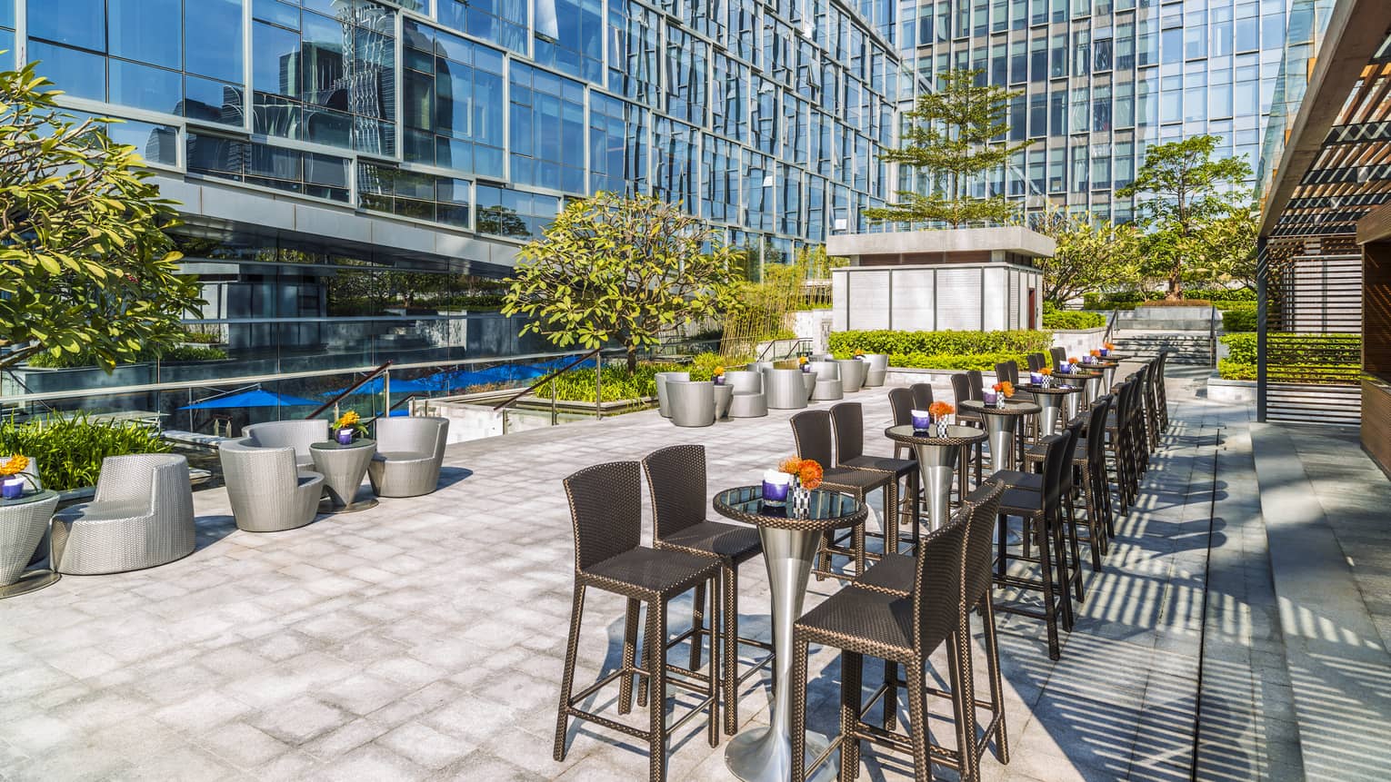 Patio tables and barstools, modern lounge chairs on sunny terrace under glass building