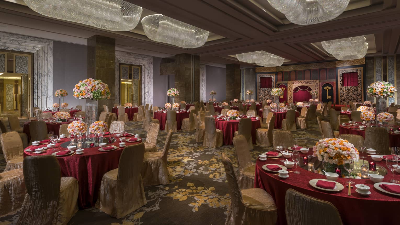 Four Seasons Ballroom with red banquet dining tables with pink flowers, long crystal chandeliers 