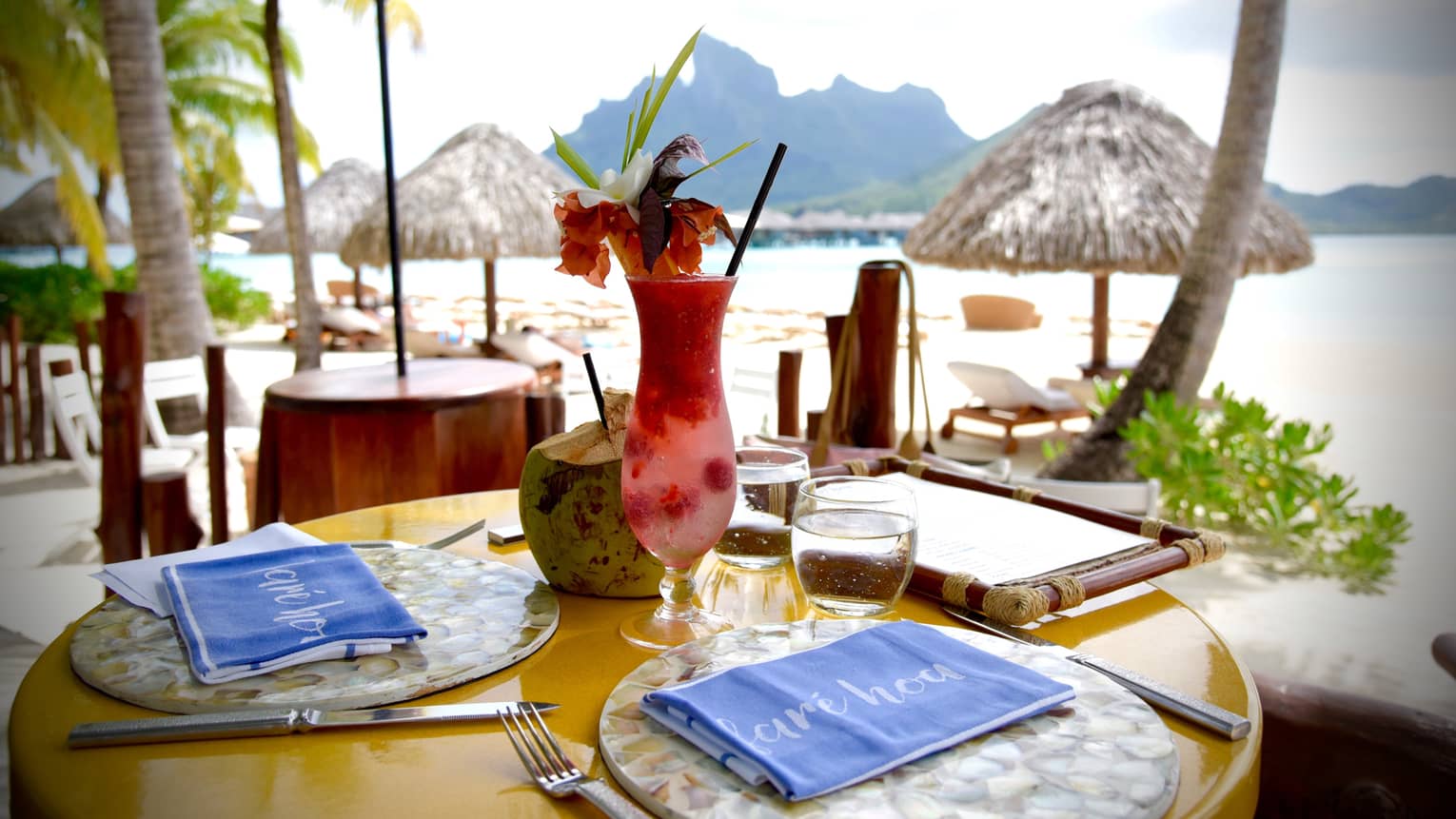Fruity cocktail with tropical flower garnish on patio dining table by Bora Bora lagoon