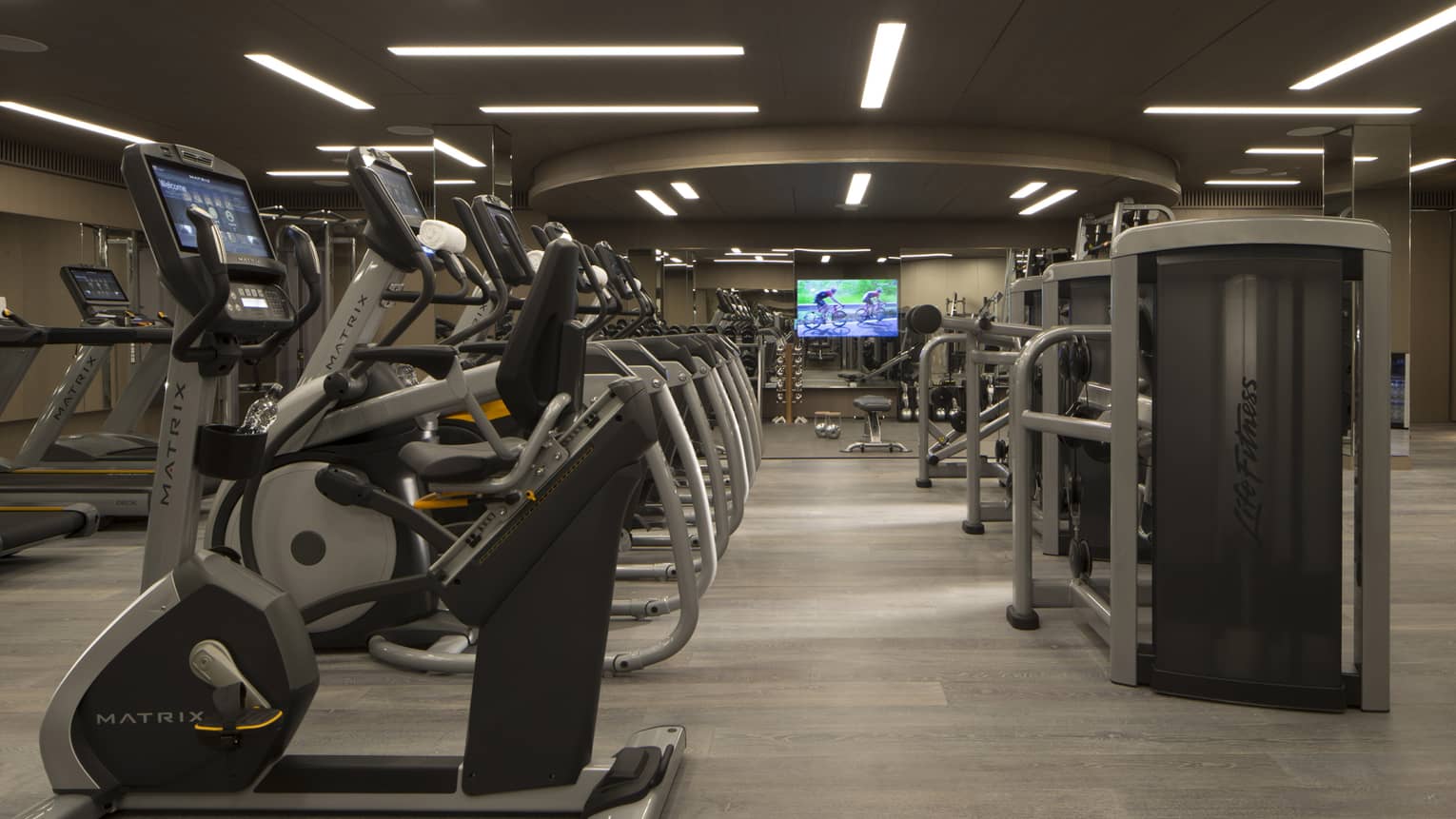 A fully-equipped gym with cardio and weight machines under dim lights.