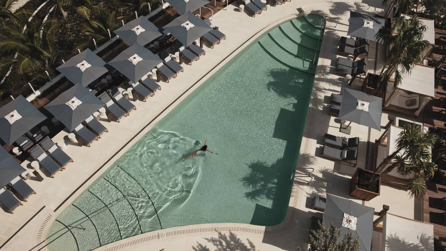 An outdoor swimming pool with grey lounge chairs and umbrellas surrounding it.