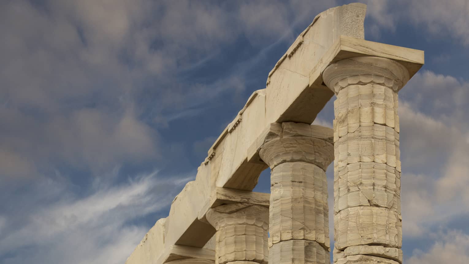 From the bottom of stairs, view of ancient towering Doric columns with vertical grooves atop a jagged brick foundation.