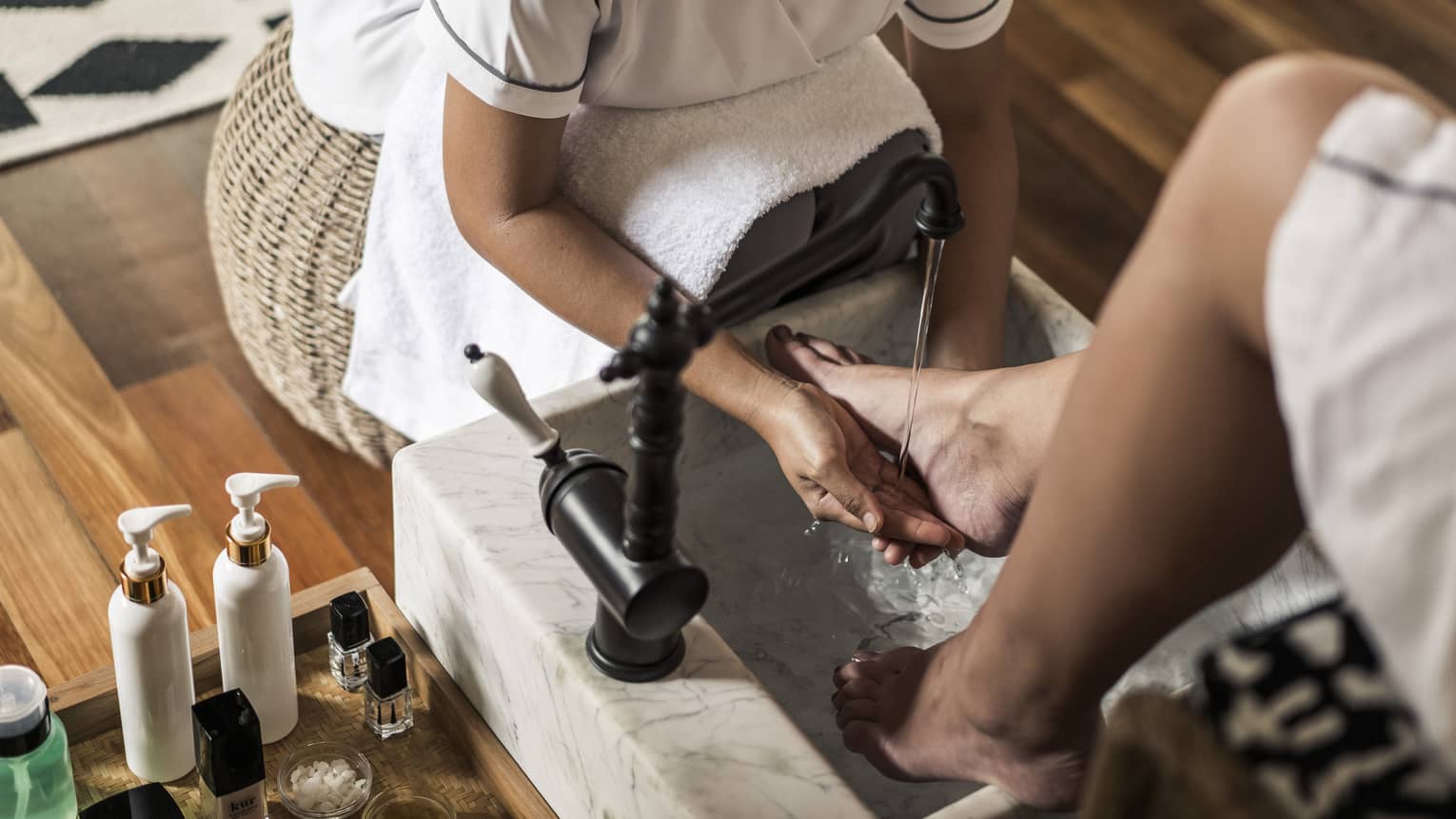 Spa staff sits on wicker stool, rinses woman's feet at pedicure station