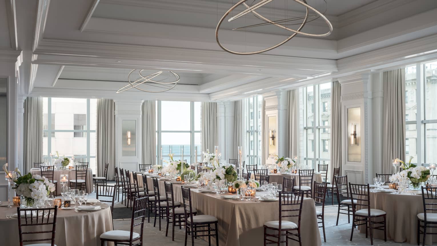 Ballroom with high ceilings and large windows, one long table surrounded by round tables