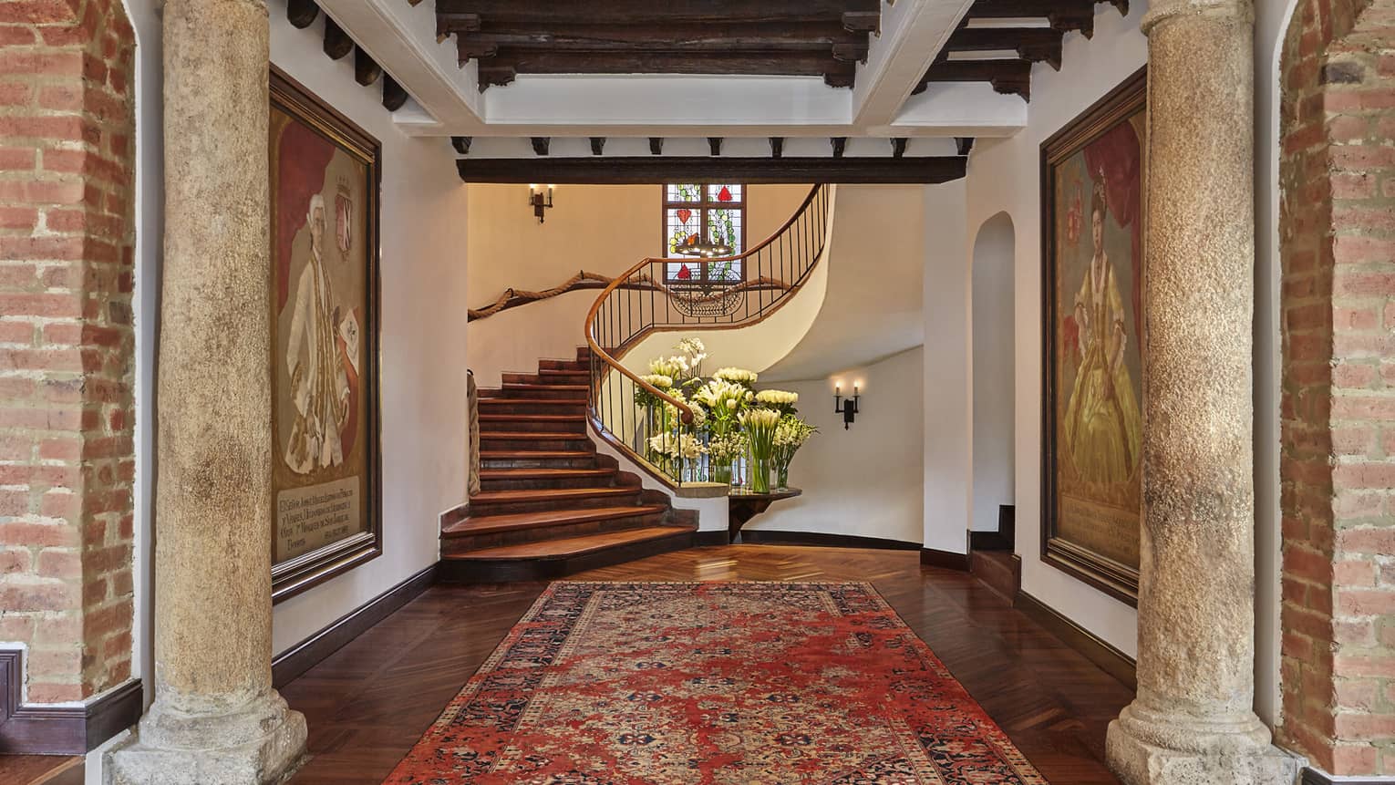 Rustic pillars, oriental carpet leading to winding staircase, table with vases with fresh white flowers