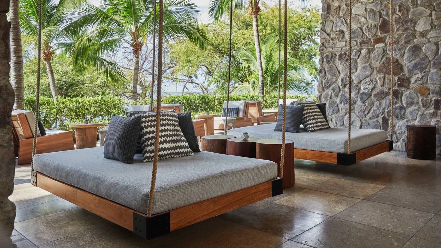 Two hanging patio beds held by ropes with thick grey cushions, accent pillows