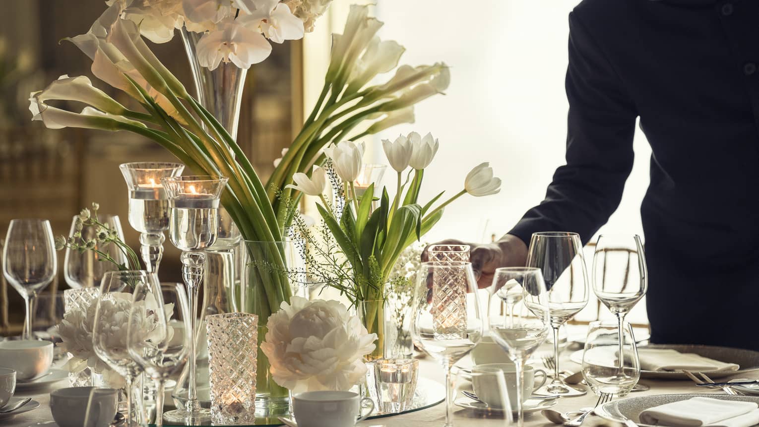 Hotel staff sets elegant banquet dining table with crystal glasses, vases with white flowers