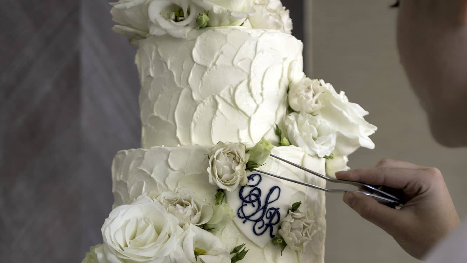 Chef places rose garnish on four tier white wedding cake