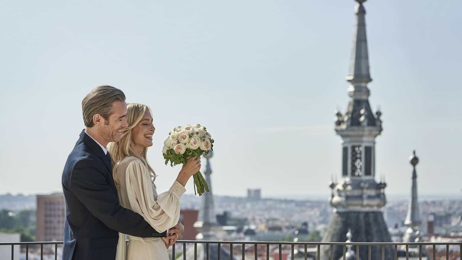 A couple embrace on a veranda overlooking several steeples in Madrid.