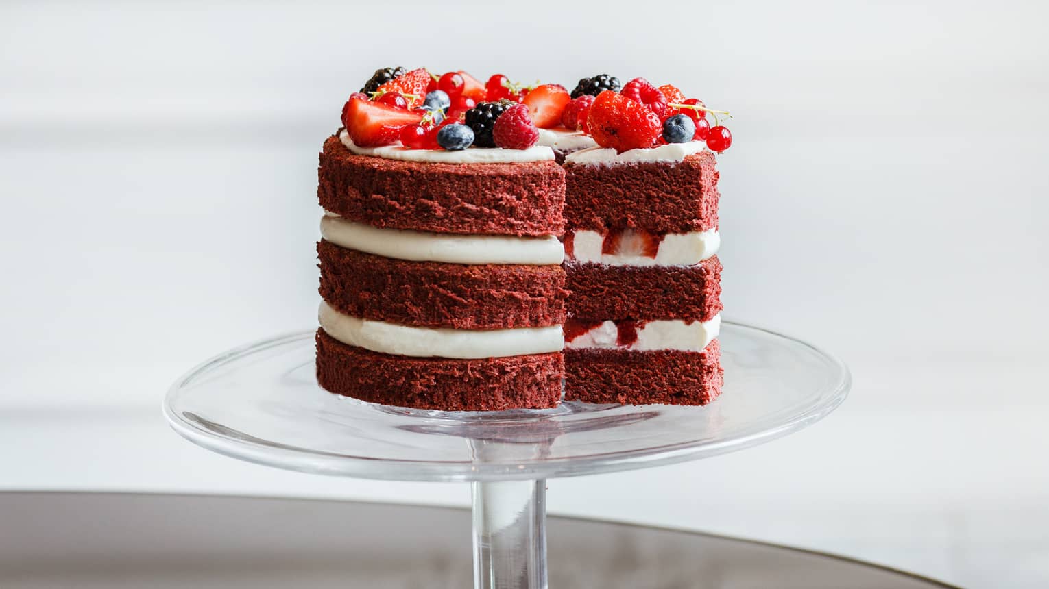 Red velvet layer cake topped with fresh berries on glass cake stand
