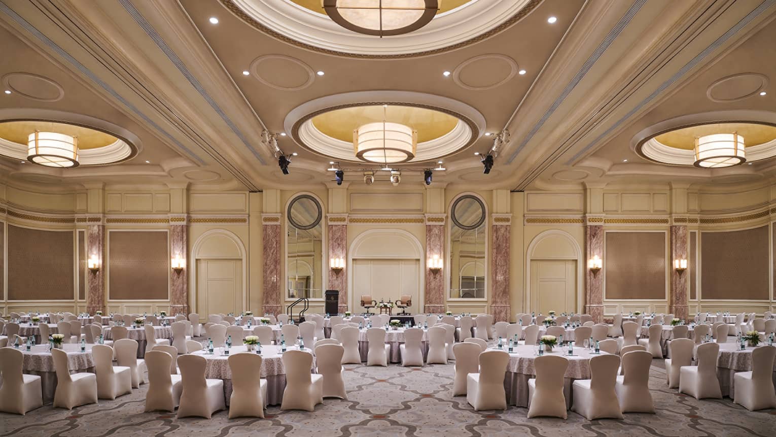 Round dining tables in large ballroom with recessed domes, large lights along high ceilings 