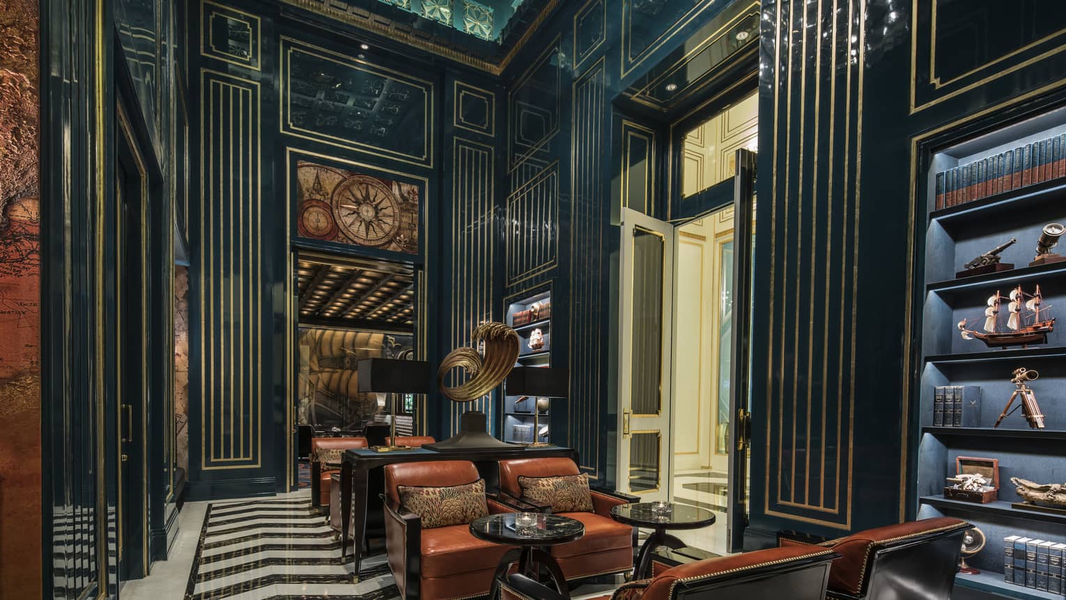The Library lounge with high ceilings, navy blue and gold walls with antique map images, cocktail tables