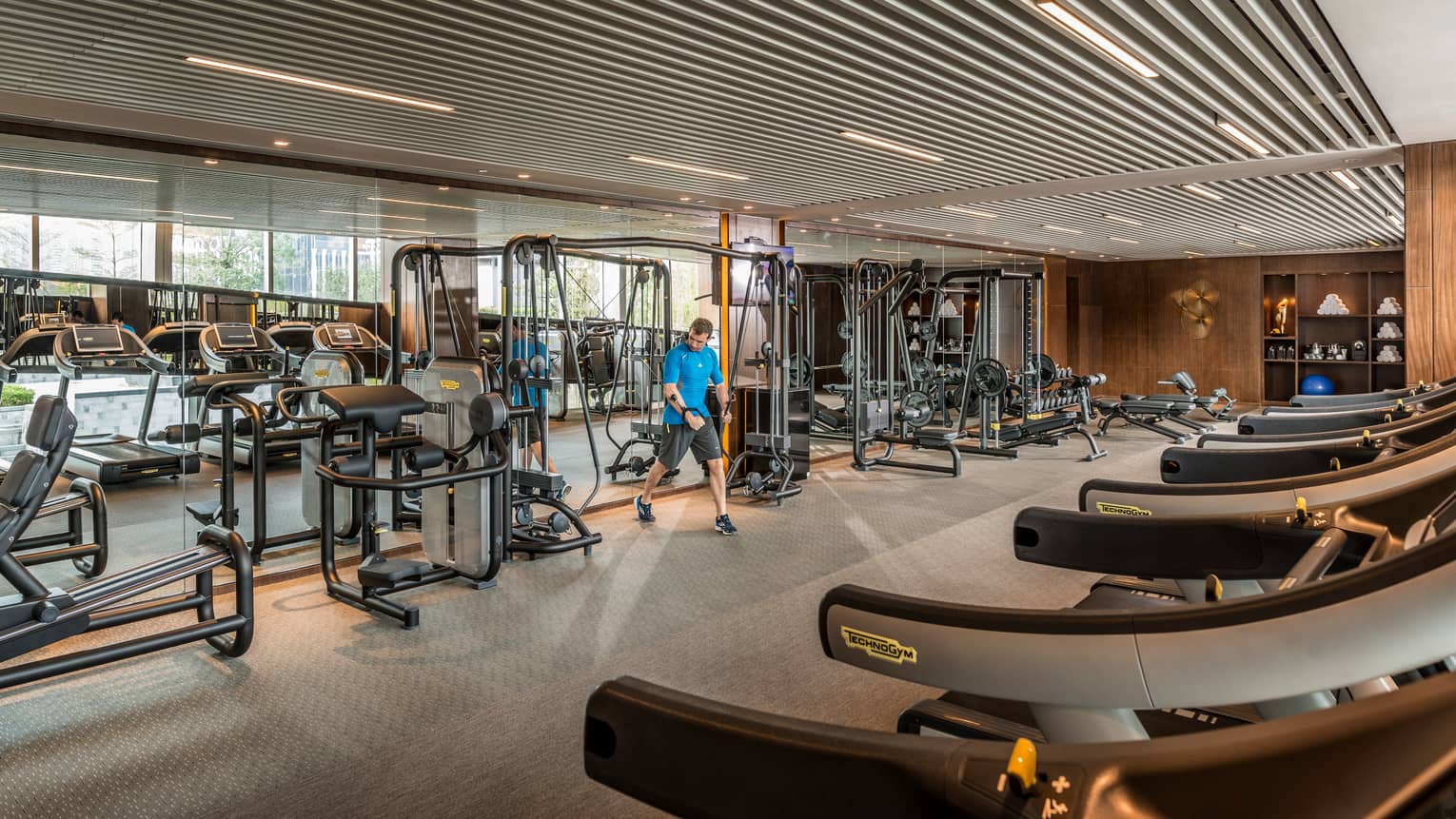 Man pulls weights machine in large Fitness Centre by mirror reflecting treadmills