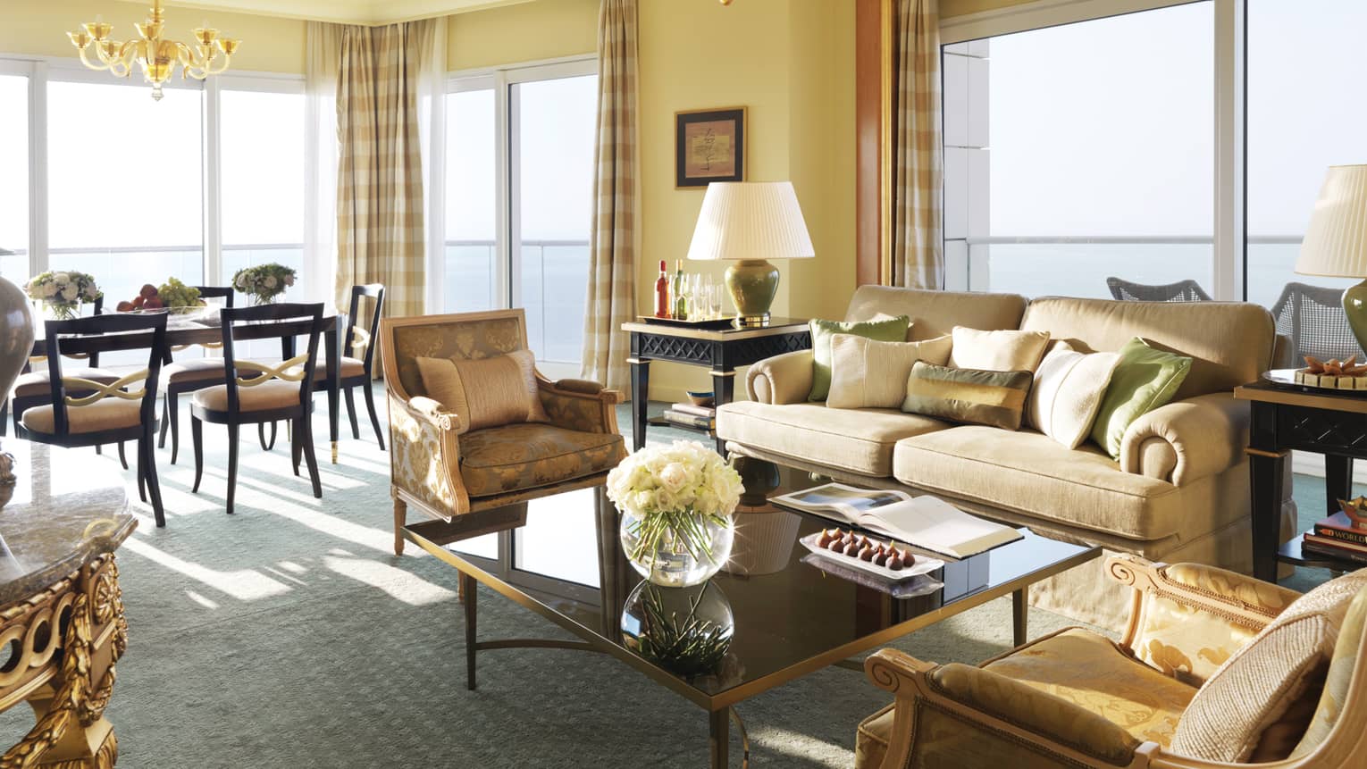 Premier Suite living room, beige sofa with green-and-gold pillows and elegant accent chairs, dining room in background
