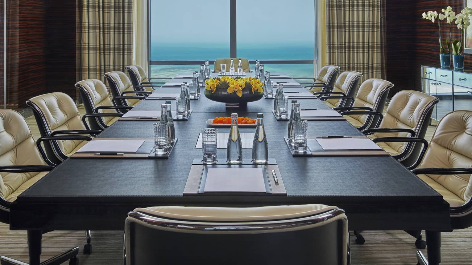Large boardroom meeting table lined with plush leather chairs in front of window with ocean view