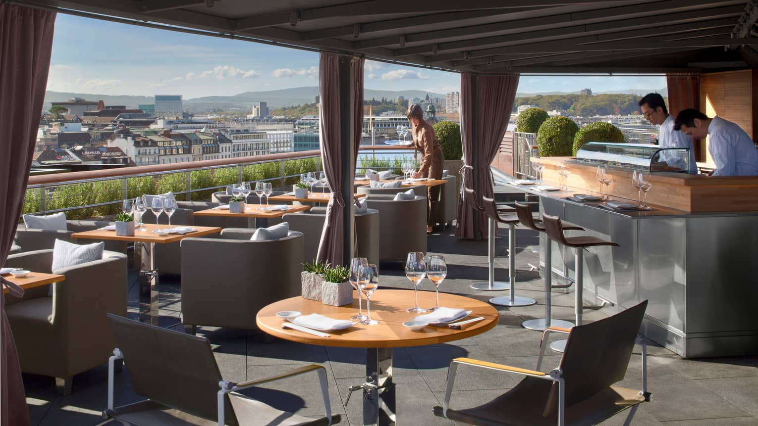 Feast on 360˚ rooftop patio dining tables and chairs under awning on sunny day, bartenders and server sets table