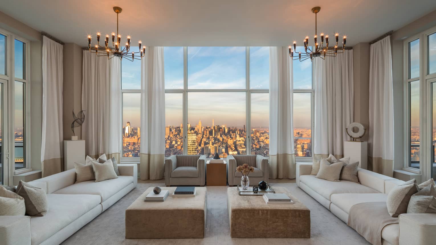 Living room with two long white sofas, armchairs around coffee tables, picture windows with city views