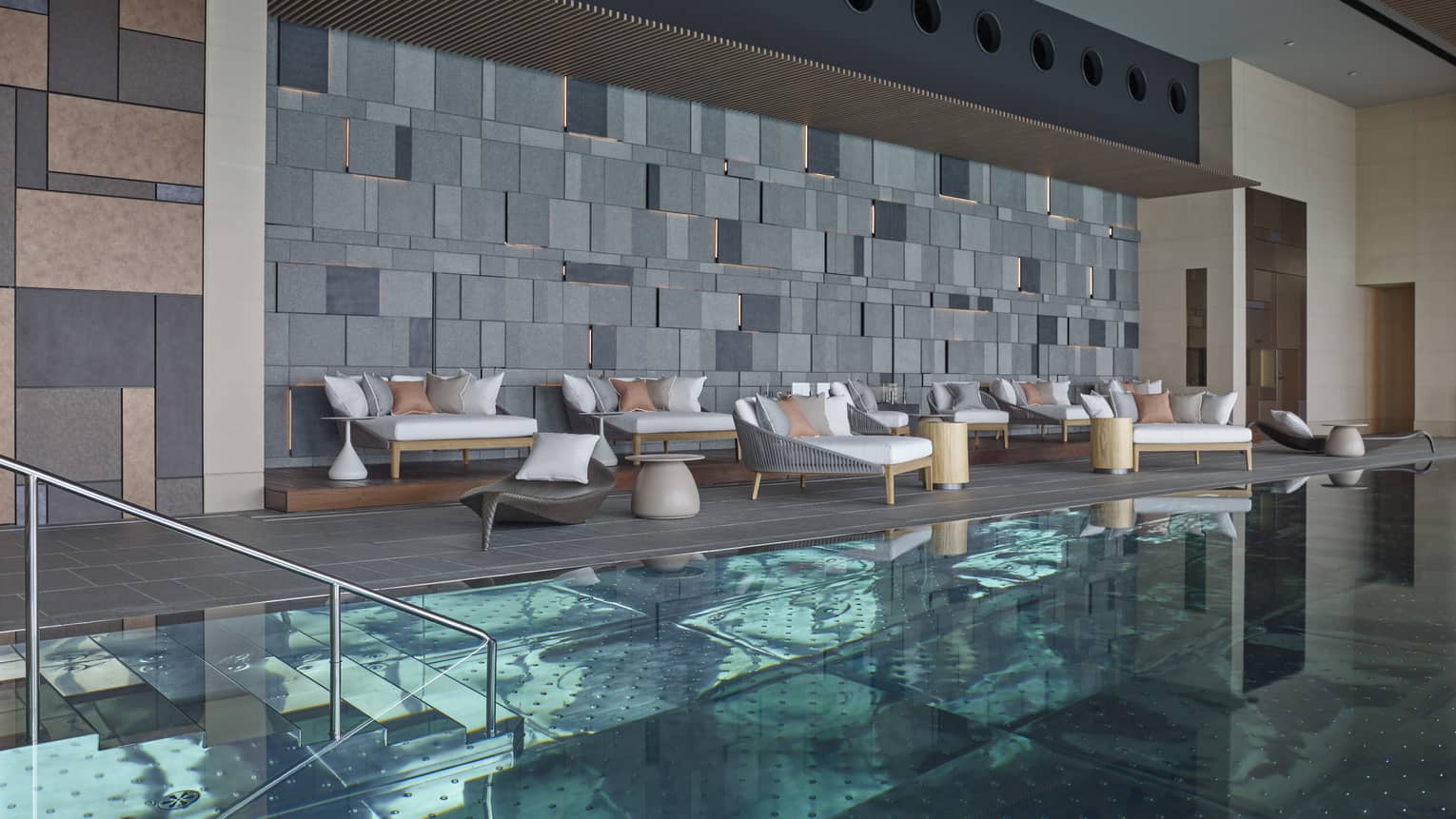 Indoor swimming pool, plush patio chairs on deck under modern brick wall