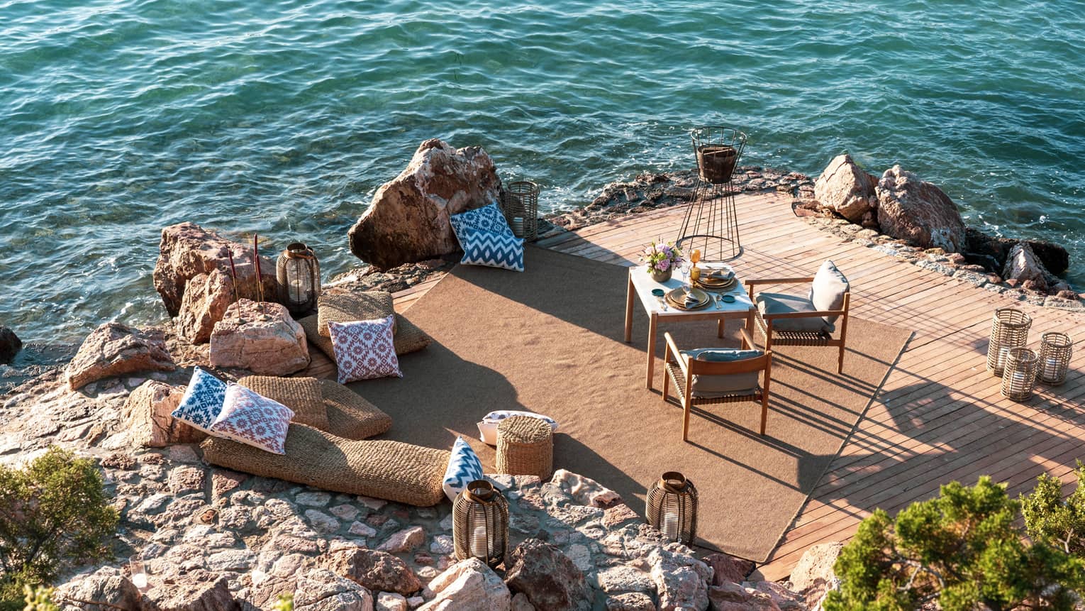 A dining table with two chairs is set on a private rocky peninsula next to the sea