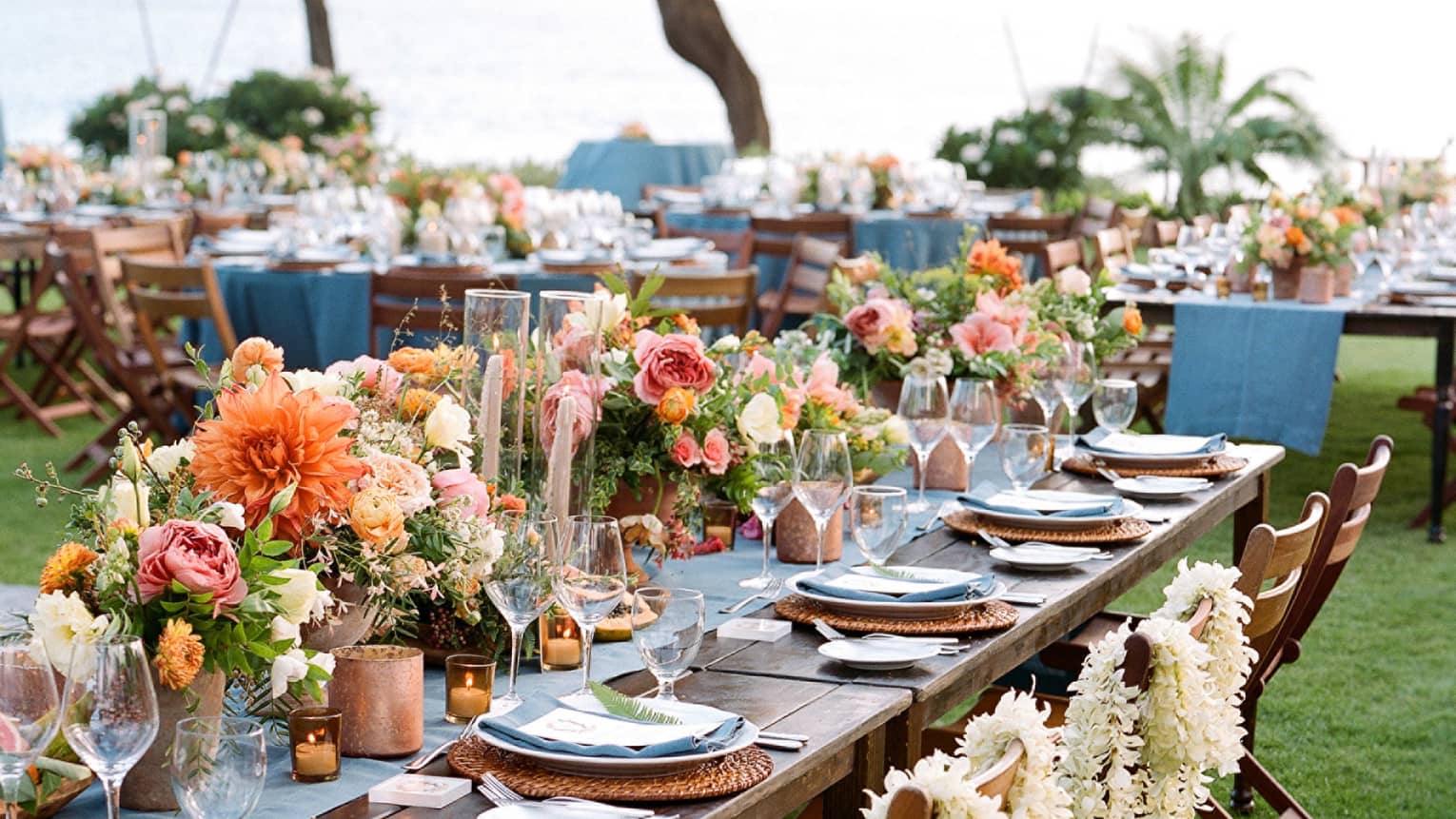 Close-up of outdoor banquet dining table with flower arrangements, white floral leis draped over chairs
